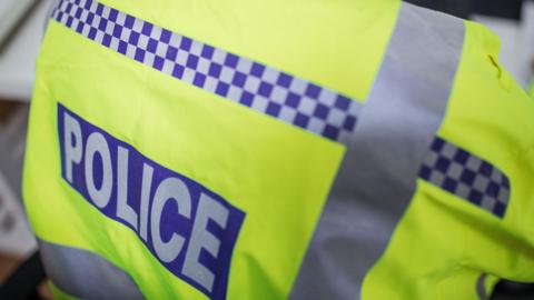 A stock picture of a police officer, who has their back to the camera and their hi-vis jacket which says "police" on the back of it.