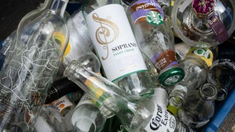 A stack of empty bottles, including a wine bottle, a beer bottle, and an iced coffee bottle, in a blue box.