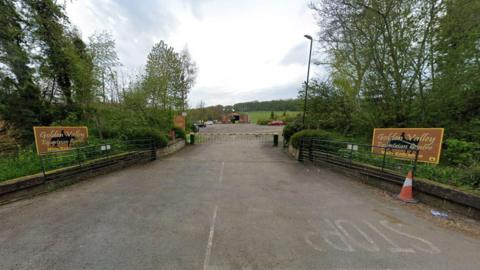 A view from the road of Golden Valley Equestrian Centre, near Alfreton, Derbyshire. There is a barrier that leads on to a car park and two signs saying Golden Valley Equestrian Centre on either side of the barrier 