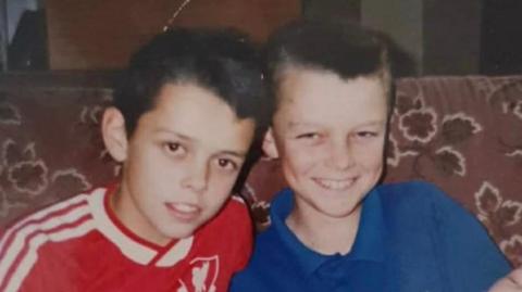 Graeme, a young boy with a Liverpool t-shirt and his brother, in a blue t-shirt, they both smile brightly.
