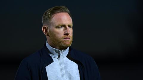 Brackley Town manager Gavin Cowan looks on from the touchline during a night game