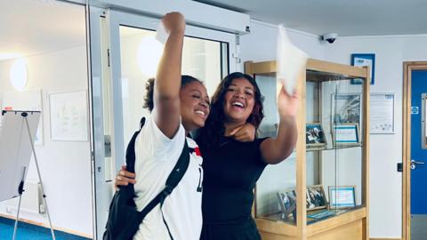 Two girls jump in the air with their GCSE results in-hand