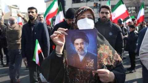 A woman holds a picture of Iran's new Supreme Leader Ayatollah Mojtaba Khamenei during a rally in Tehran. Iranian flags are seen in the background. Photo: 9 March 2026