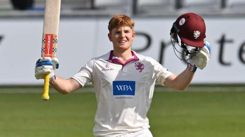 Thomas Rew raises his bat and helmet to celebrate scoring his maiden century