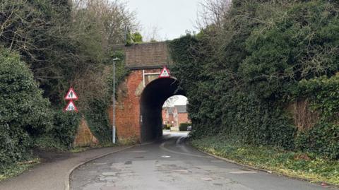 A stretch of road with road signs and a bridge with a tunnel underneath it