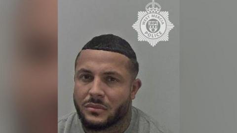 A police mugshot of Esten Bennett. He has short black hair and black facial hair.