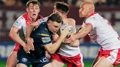 Hull KR players Jack Broadbent, Tom Davies and Dean Hadley tackle Wigan's Jai Field as he breaks with the ball in his left hand