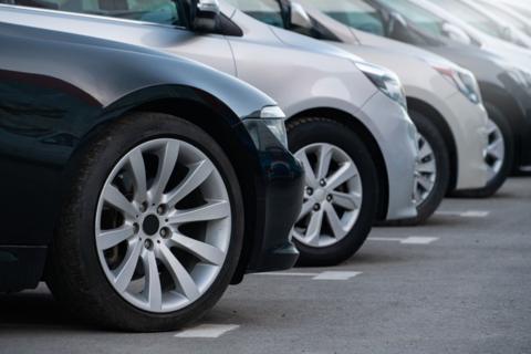 A closeup of the fronts of several cars parked pointing to the right of the image. The cars are a mixture of black, silver and white.