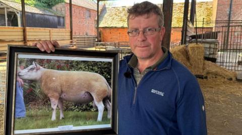 Farmer David Thornley holds a framed picture of one of his prize-winning rams