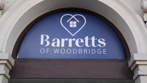 A white and blue semi-circle sign above a doorway of a shop. It reads "Barretts of Woodbridge". 