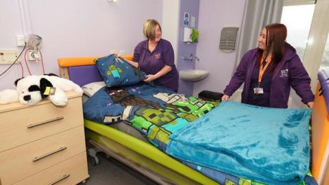 Two nurses stand by a bed