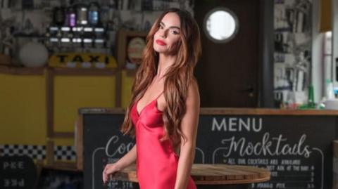 Hollyoaks character Mercedes McQueen played by actress Jennifer Metcalfe is seen in a red dress in a bar.