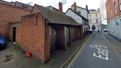 Red brick building with three silver metal doors located in a back street.