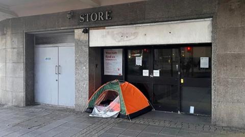 A green and orange tent in the doorway of an abandoned shop.