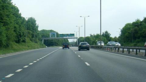 A dual carriageway with two cars on and a slip road to the left. 