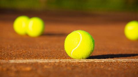 A clay tennis court with a number of bright yellow balls scattered about