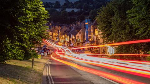 High street traffic at night in Burford with red streaks of light creatively travelling through the streets.