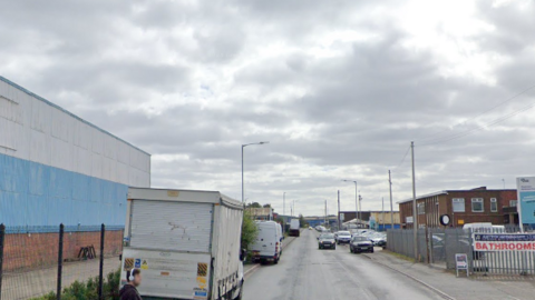Vehicles are parked on either side of the road which runs through a partial industrial estate.