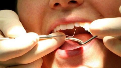 A person with their mouth open and the dentists hands holding dental equipment