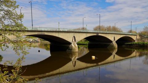 A plain three-span concrete bridge with Art Deco embellishments and some greenery visible on either bank of the river.