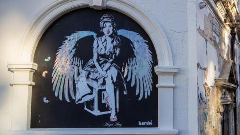 Black and white painting of Amy Winehouse with angel wings on the wall of Koko