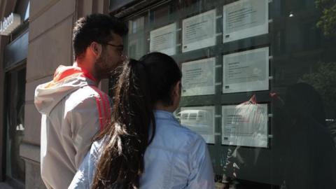 Two people look at job announcements in the window of an agency in Naples