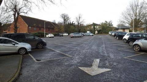 A car park in Diss. Cars can be seen parked in spaces and white road markings.