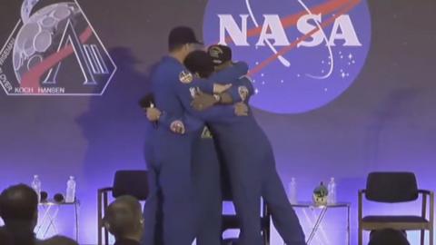 Artemis II astronauts hug on stage wearing blue overalls
