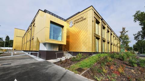 The University of Worcester's Three Counties Medical School. It is a yellow building with the university logo and crest on the side.