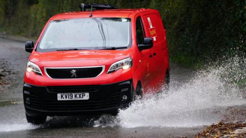 A Royal Mail van drives through a puddle