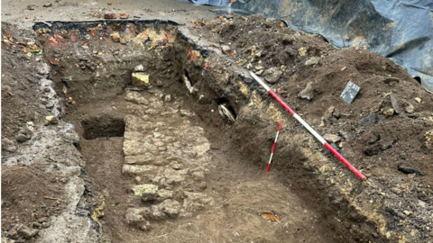 A dug out trench with old structural remains of a stone wall.