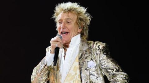 Rod Stewart on stage in Stockholm on 4 June 2024. He is wearing a gold blazer and holding a microphone 