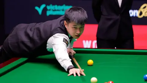 Zhao Xintong of China plays a shot in the second round match against Ding Junhui of China