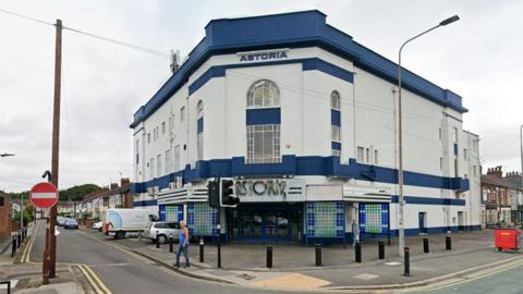Exterior of the Astoria Bingo Club a large Art Deco former cinema which is painted white with dark blue strips along its roof and above the main door. It is located on a corner site on Holderness Road and Lake Drive
