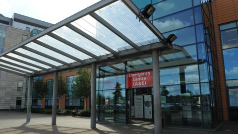 The Peterborough hospital emergency department building - with a glass frontage and glass door and a red emergency sign board.