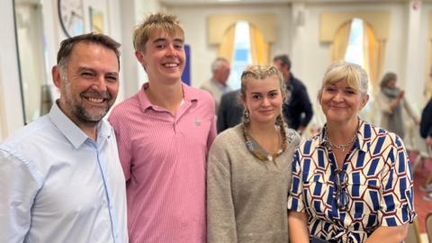 A man, a teenage boy, a teenage girl and a woman standing next to each other and smiling