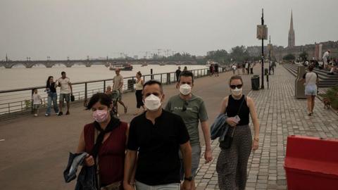 People wearing masks to protect themselves from smoke walk along the river in central Bordeaux. The sky is very hazy.