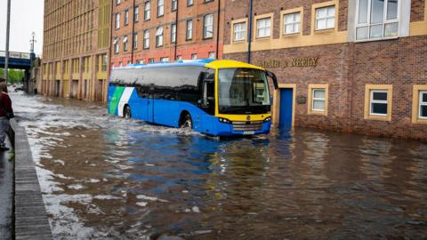 A bus drives through a heavily flooded street