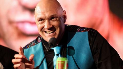 Tyson Fury in a blue suit speaks at a news conference