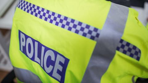 The back of a police officer wearing a high-visibility jacket with a police label on.