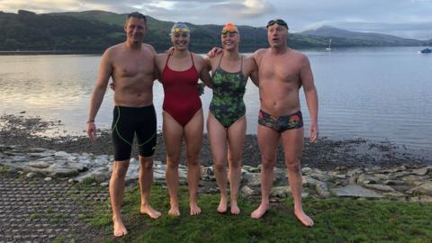 Team photo of the four adventurers in their swimming gear at the end of the challenge at Lake Bala in Wales