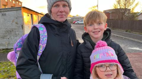 Annika and her children are standing in a street wearing winter jackets and colourful woolly hats. 
