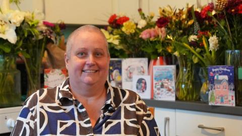 Clare Jones yn ei chartref wedi ei hamgylchynu gan gardiau a blodau