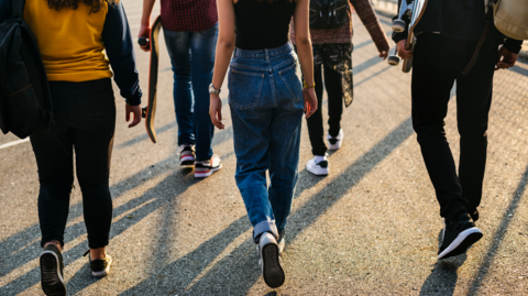 Rear view of a group of school friends walking outdoors dressed in  jeans and trainers