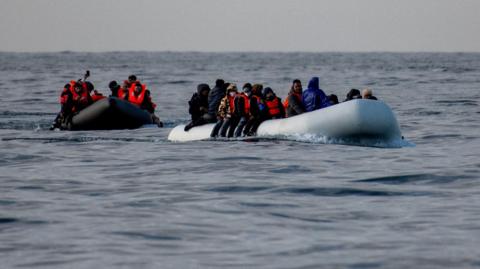 Two rubber dinghies full of people wearing life jackets. 