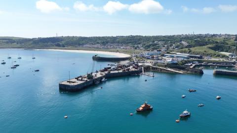 An aerial view of Alderney Harbour. The water is blue and there are boats on the water. 
