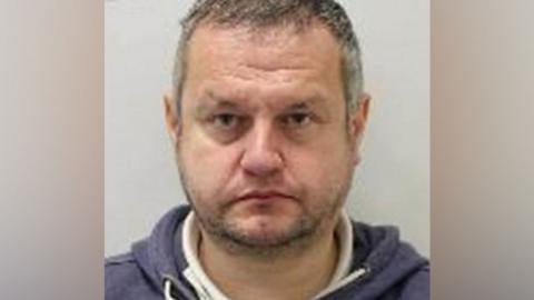 Gareth Viccars is seen in a police custody shot looking at the camera. He has short greying hair and a stubbly beard and moustache. He is wearing a dark blue and white hoodie