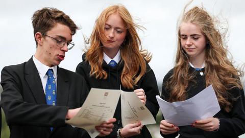 a boy and two girls in school uniform look at their exam certificates