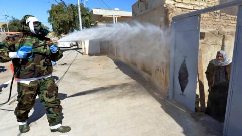 An Iraqi man looks out of a doorway as a civil defence worker disinfects an area of Najaf where Covid-19 cases have been detected (3 February 2020)