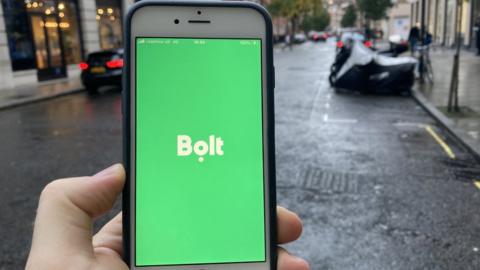 Bolt app on a mobile phone in foreground, car in background